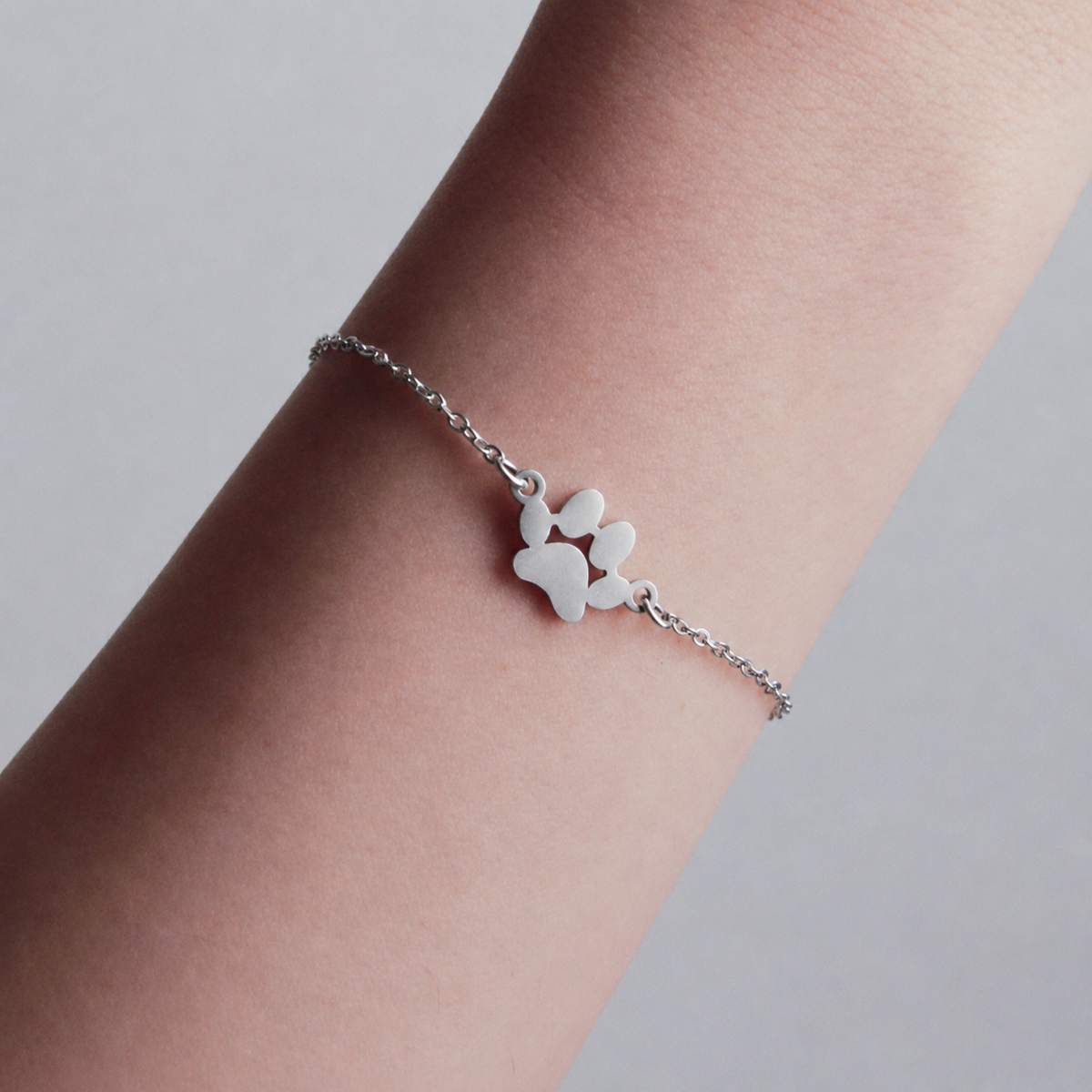 Silver bracelet with a paw print charm on a wrist against a neutral background