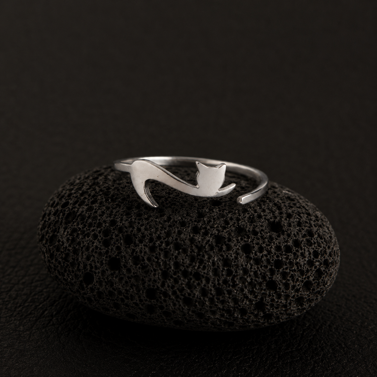 Curious Tail Cat Ring in silver-plated finish displayed on a black lava stone against a dark luxury background.