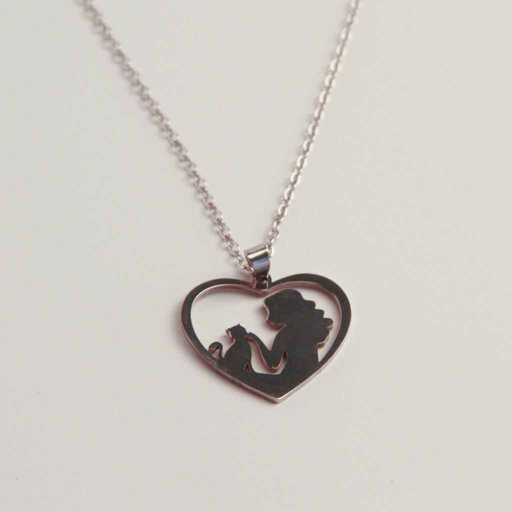 A silver heart-shaped pendant necklace featuring a silhouette cutout of a woman holding a child, displayed on a clean white background.