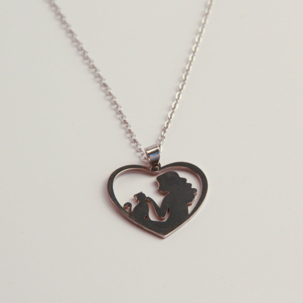 A silver heart-shaped pendant necklace featuring a silhouette cutout of a woman holding a child, displayed on a clean white background.