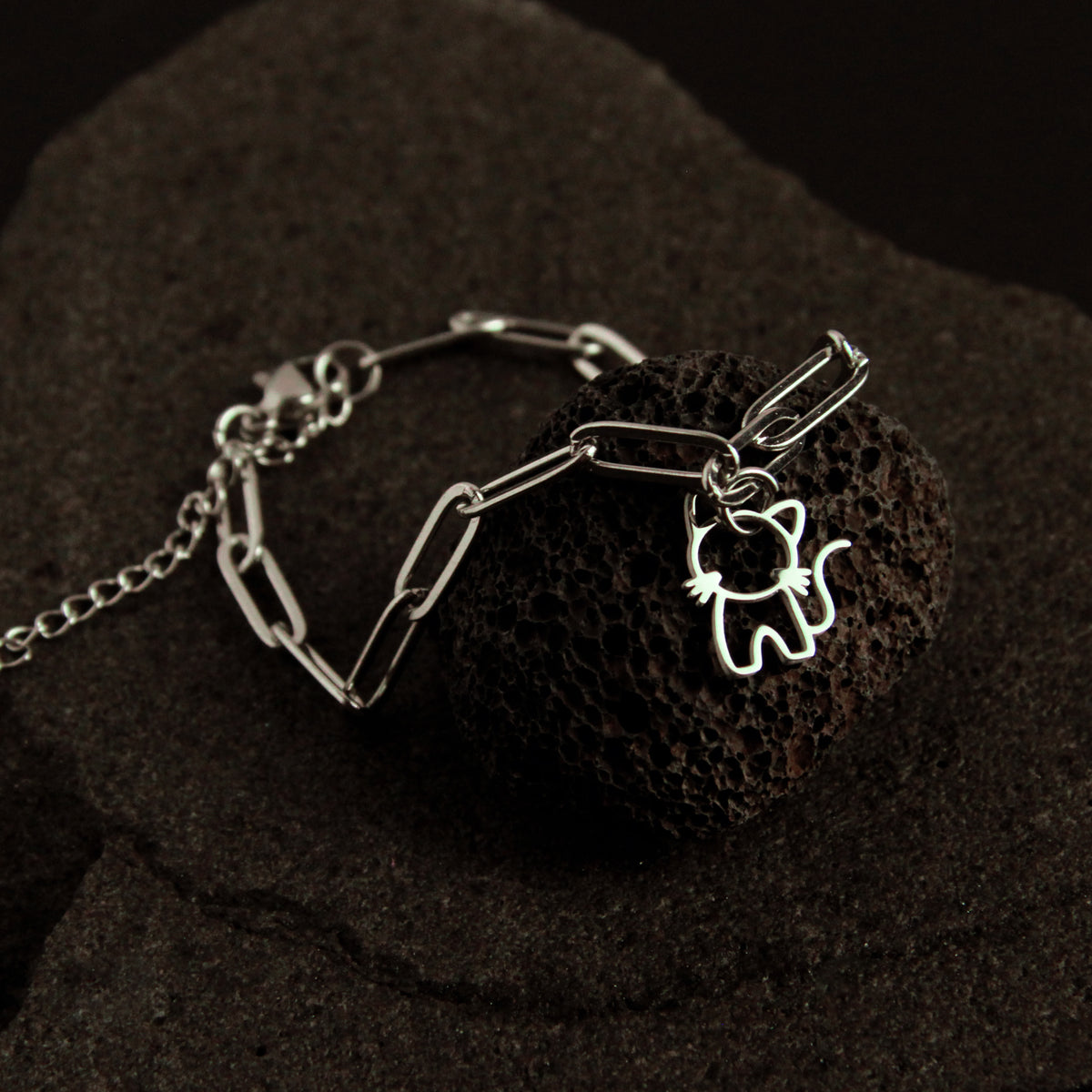 Silver bracelet with a cat-shaped charm on a dark textured surface