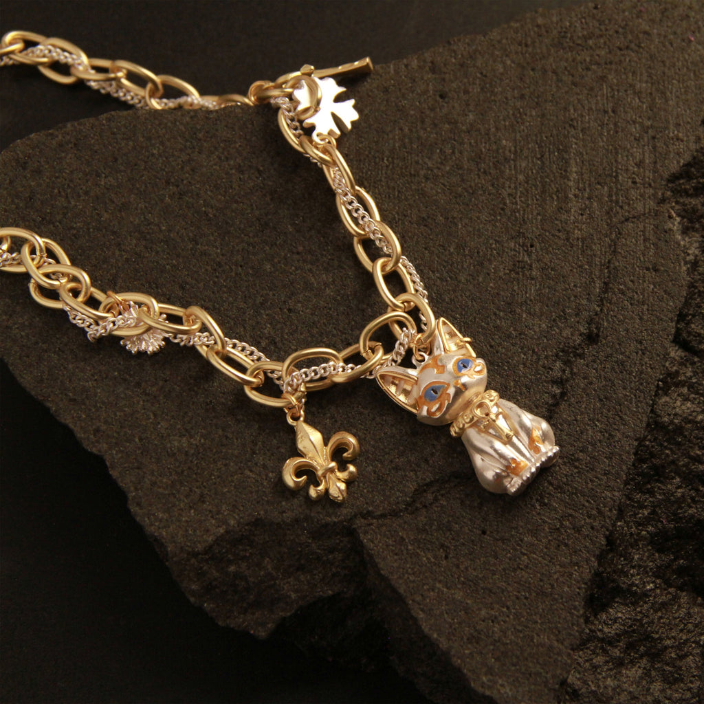 Gold bracelet with cat and fleur-de-lis charms on a dark stone surface