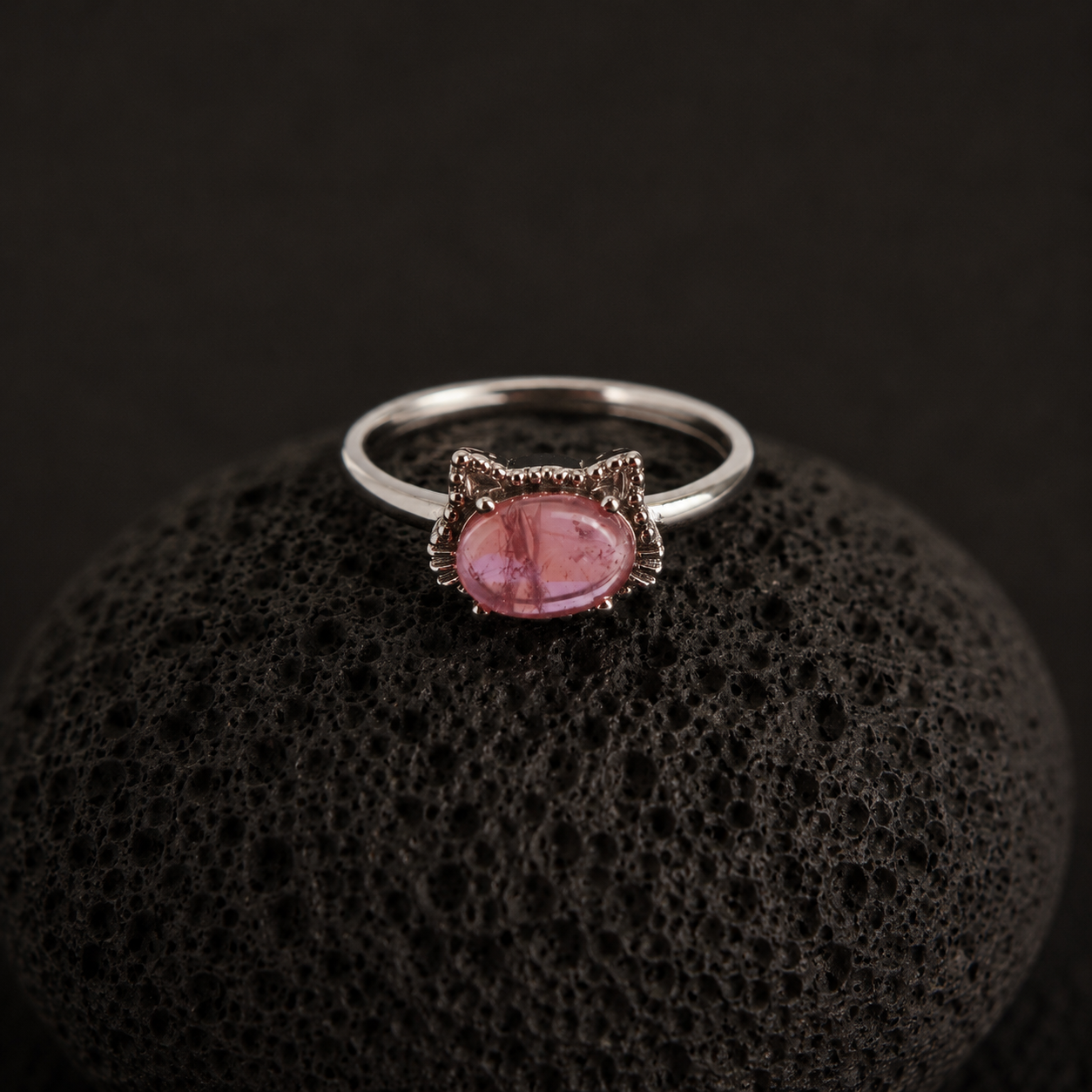 Close-up angled view of the adjustable Rose Quartz Cat Ring on a black lava stone.