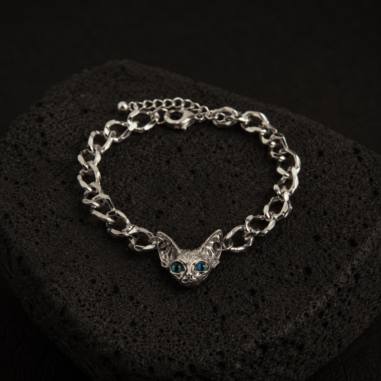 Silver-plated Sphynx Guardian Bracelet with a blue-eyed sphynx cat charm displayed on a black lava stone.
