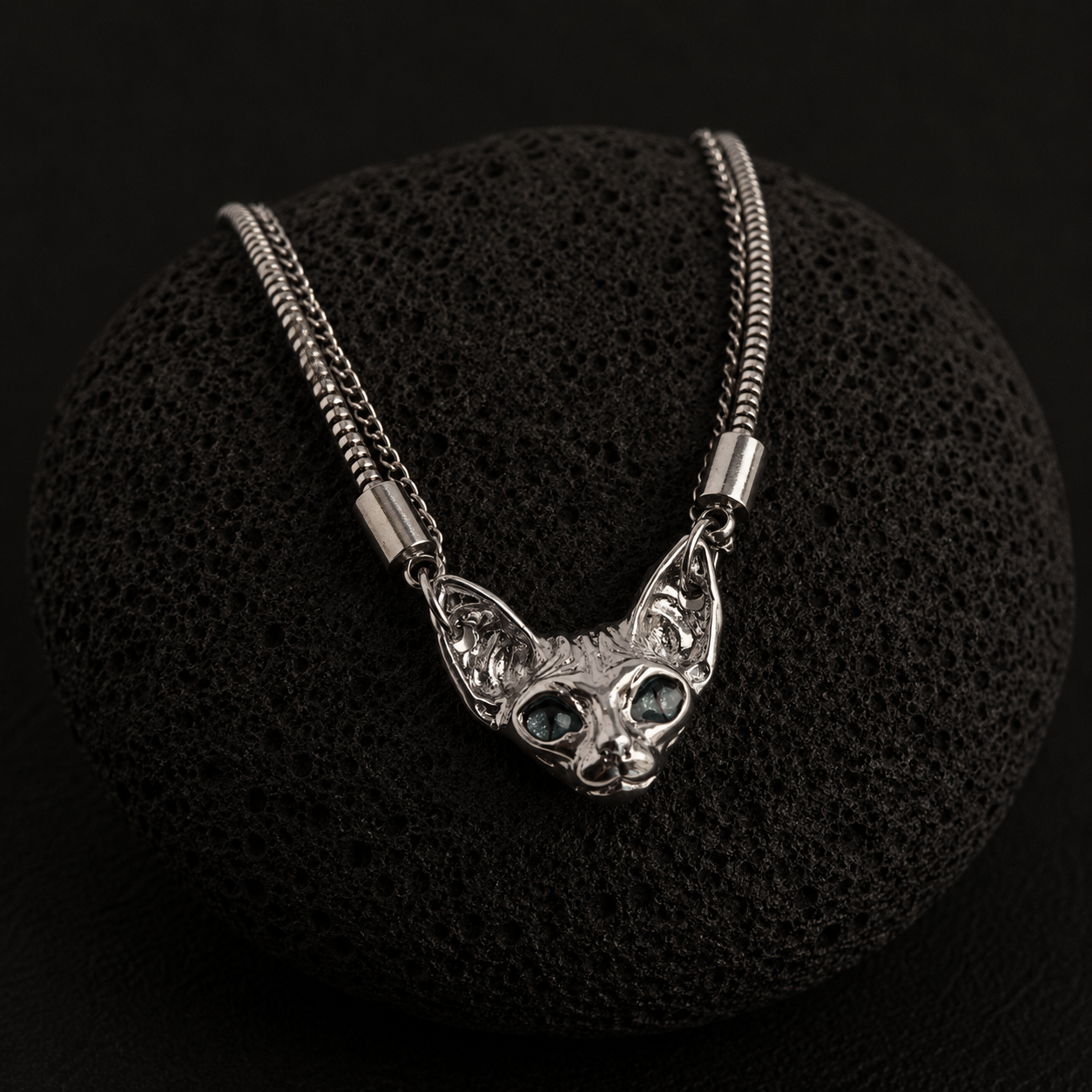 Silver-plated Sphynx Guardian Necklace with a blue-eyed sphynx cat pendant displayed on a black lava stone.