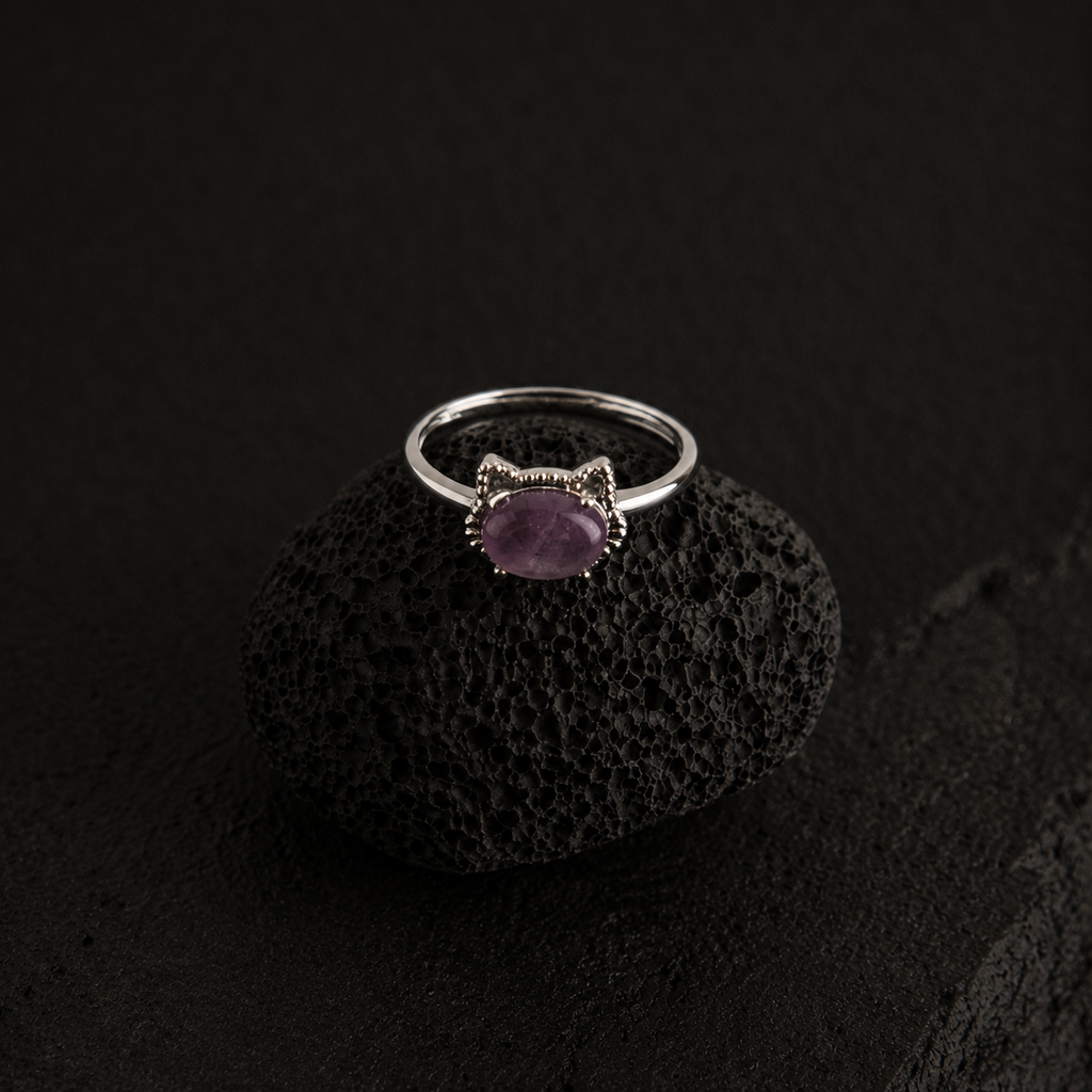 Silver cat ring with a purple gemstone on a black textured surface