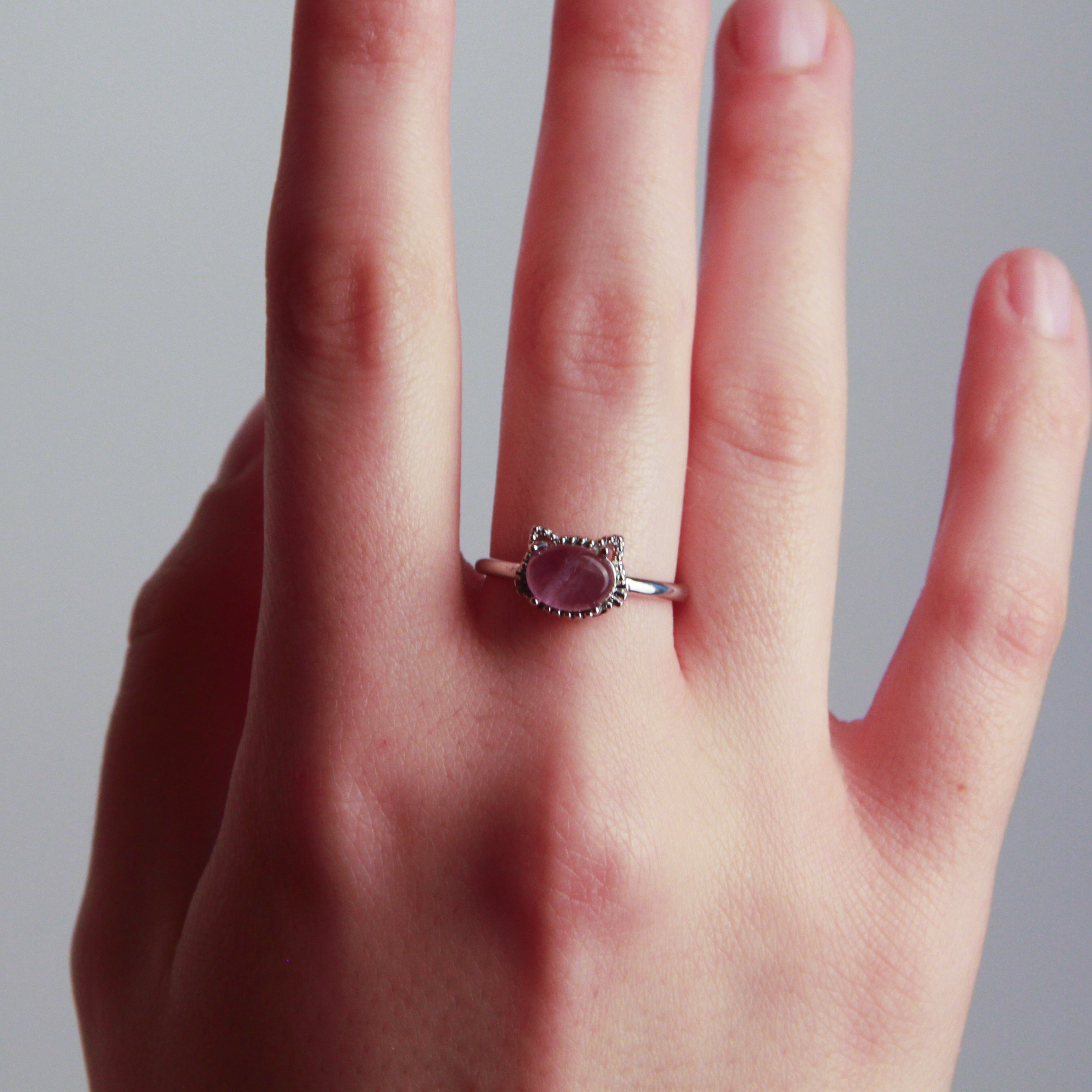 Hand wearing a cat ring with a pink stone on a neutral background