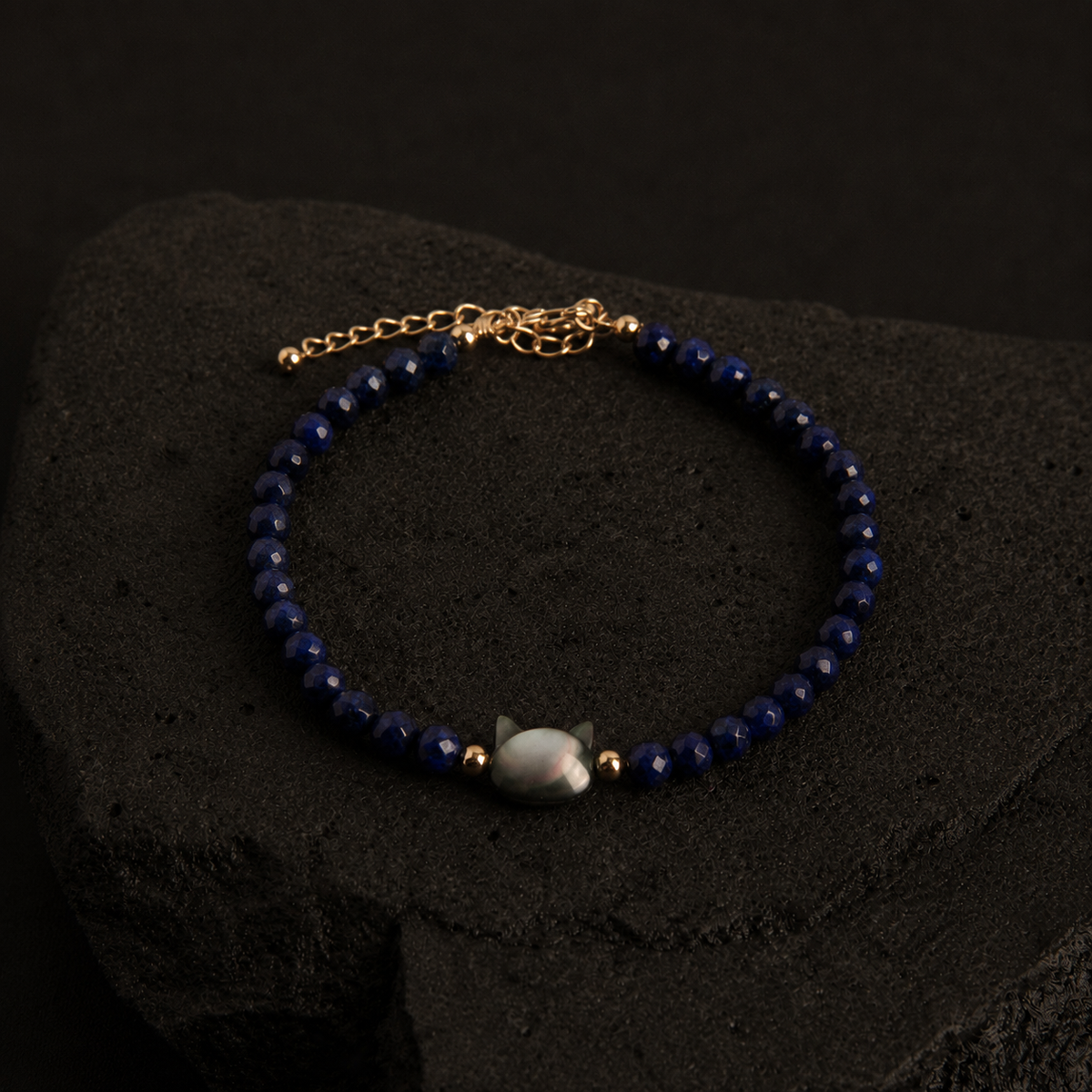 Blue faceted bead bracelet with an iridescent cat charm and gold accents.