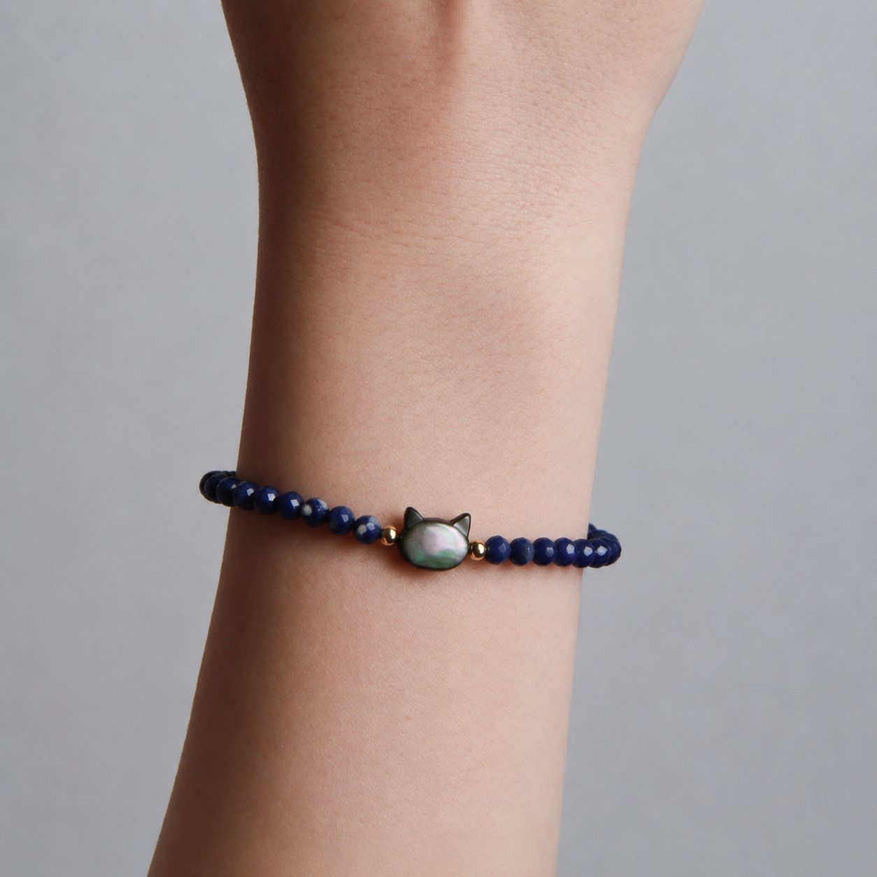 Blue faceted bead bracelet with an iridescent cat charm and gold accents.