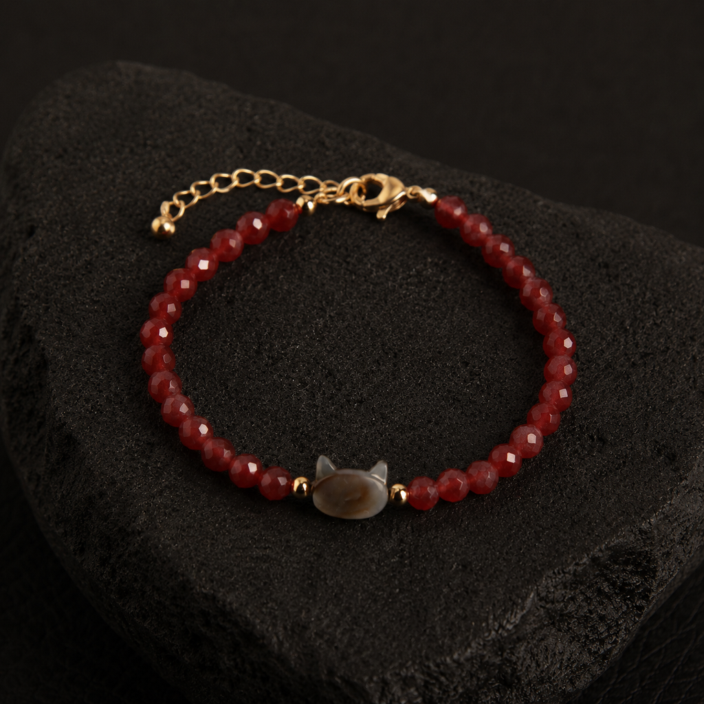 Red faceted bead bracelet with a cat charm and gold accents displayed on a black textured stone.