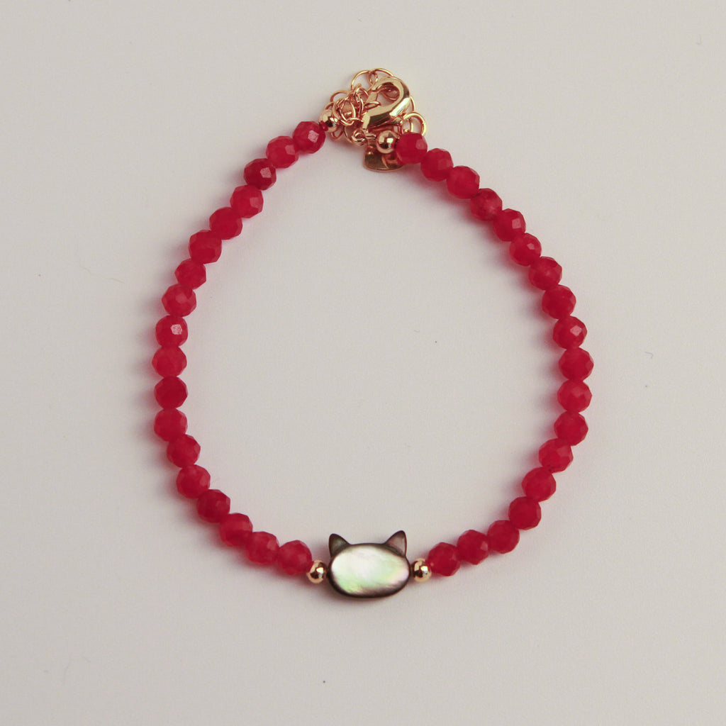 Red faceted bead bracelet with a cat charm and gold accents displayed on a black textured stone.