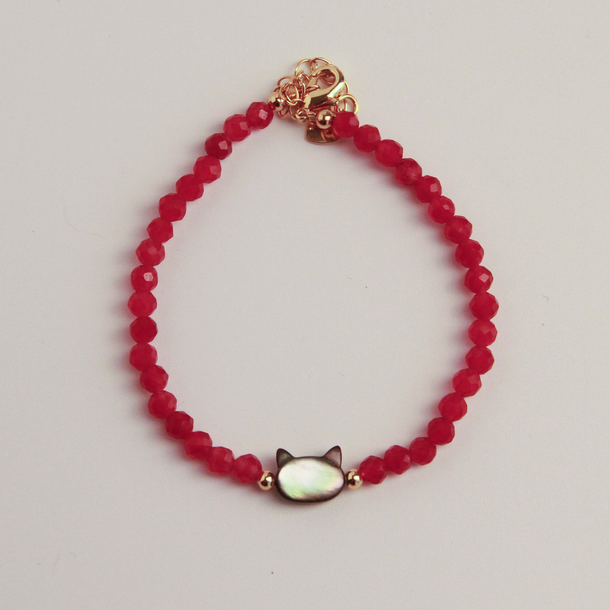 Red faceted bead bracelet with a cat charm and gold accents displayed on a black textured stone.