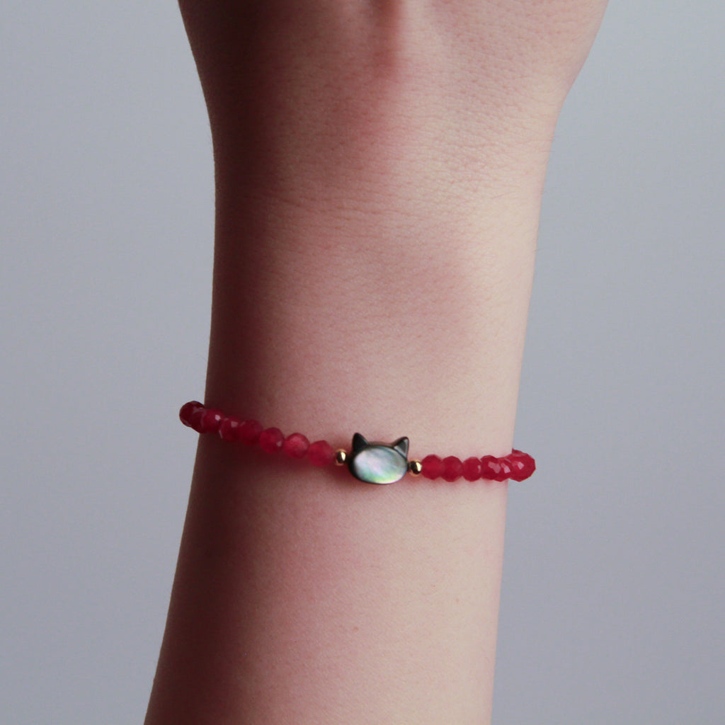 Red faceted bead bracelet with a cat charm and gold accents displayed on a black textured stone.
