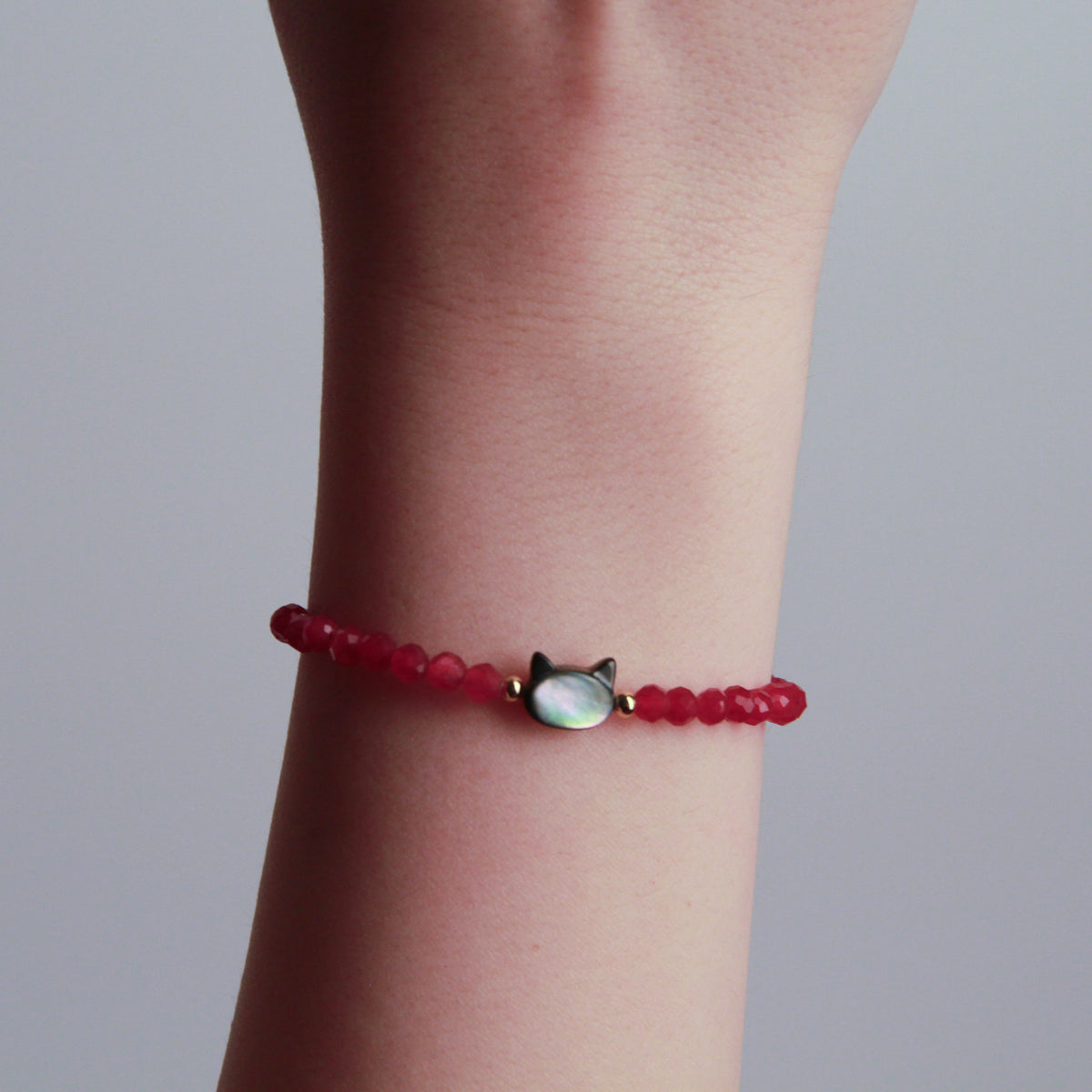 Red faceted bead bracelet with a cat charm and gold accents displayed on a black textured stone.