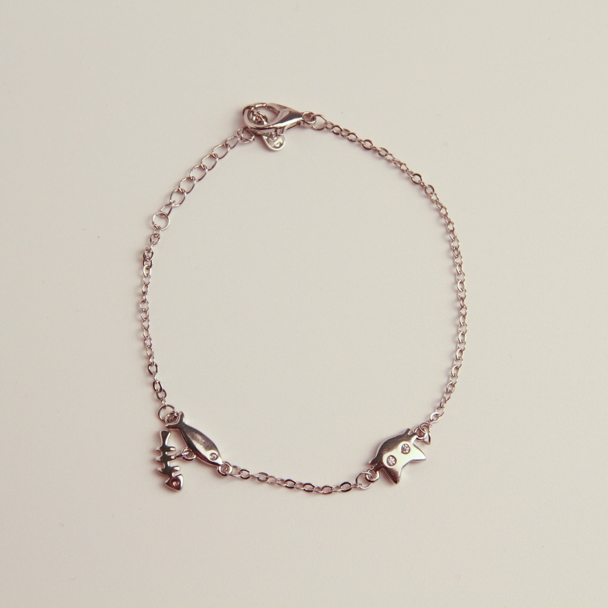 Silver cat charm bracelet with fishbone and fish charms on a delicate chain.