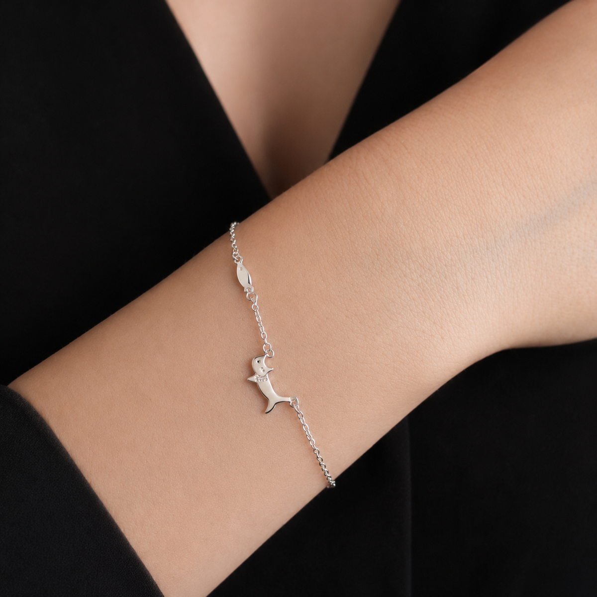 Silver bracelet with a cat design on a person's wrist against a black background