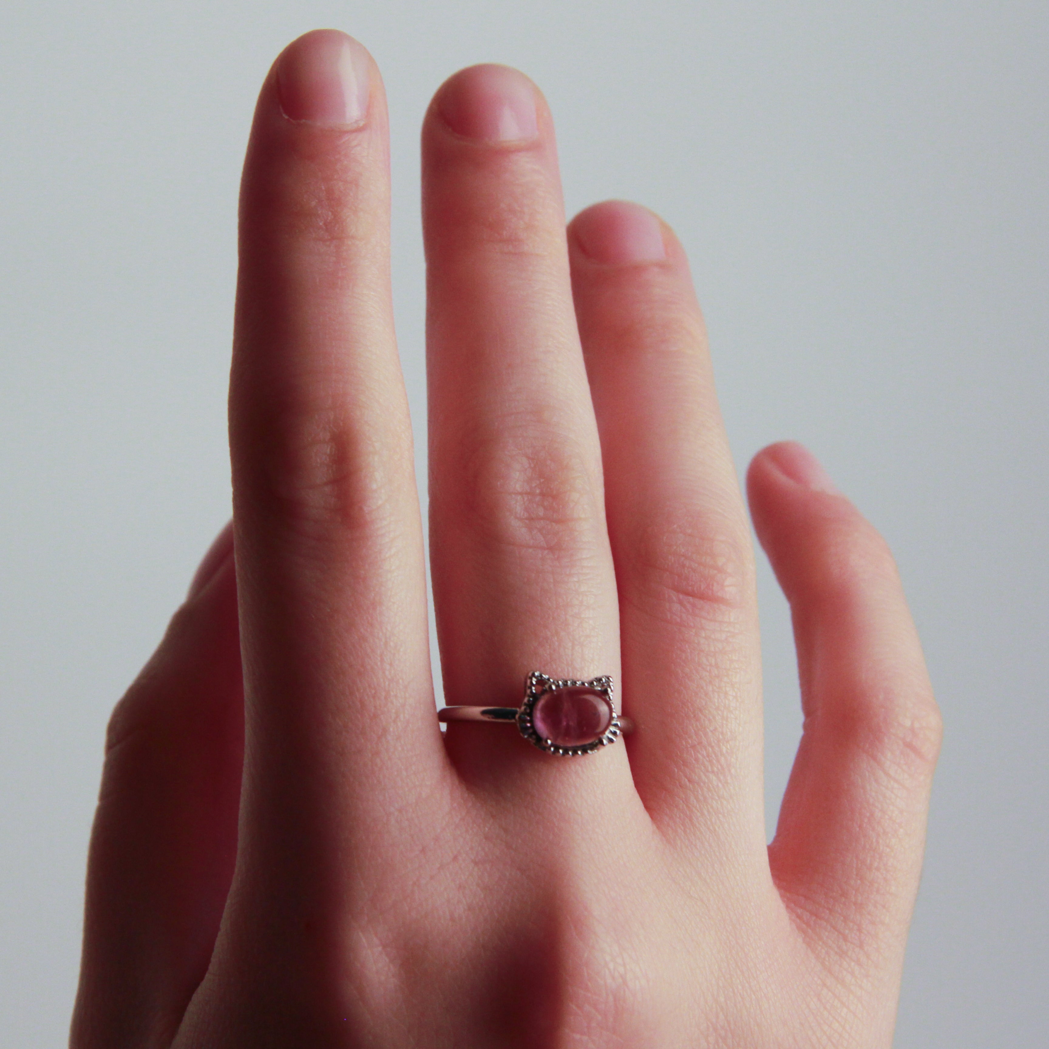 Hand wearing a cat ring with a pink gemstone on a plain background