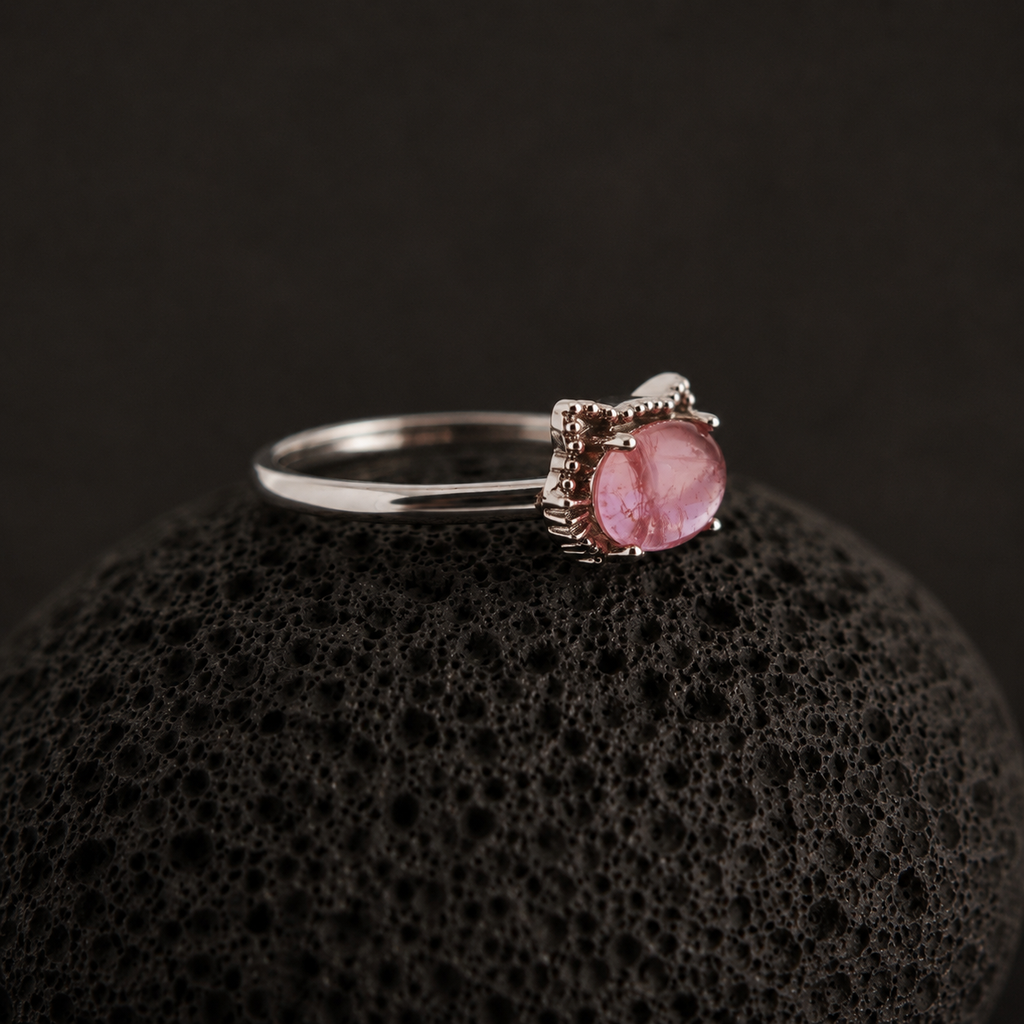 Silver ring with a pink gemstone on a black textured surface