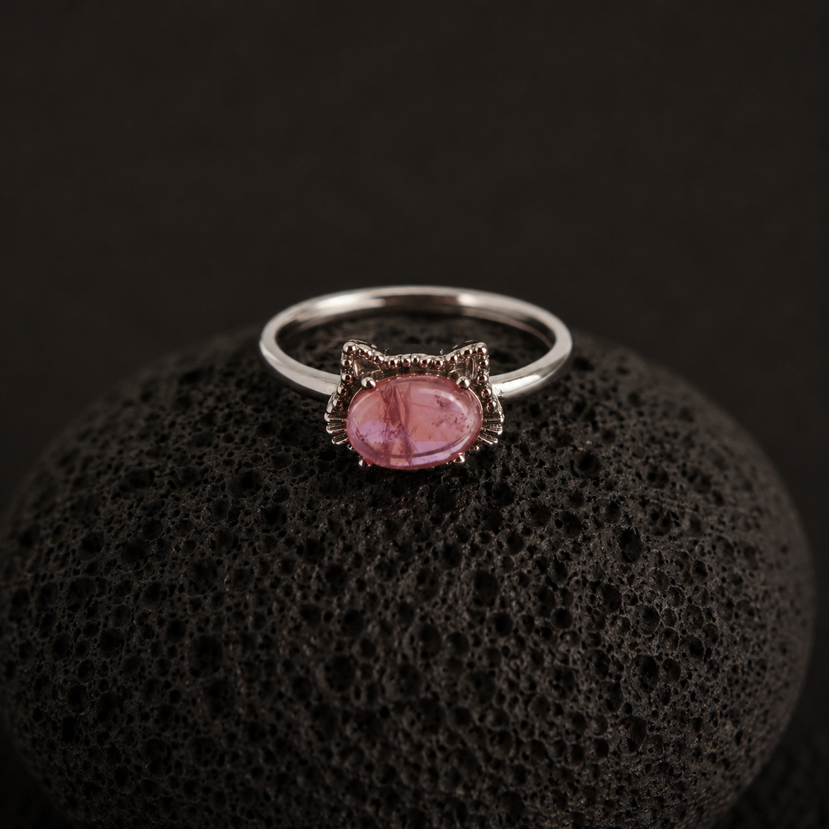 Silver ring with a pink gemstone on a black textured surface